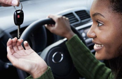 teen girl being handed the keys to the while sitting behind the wheel