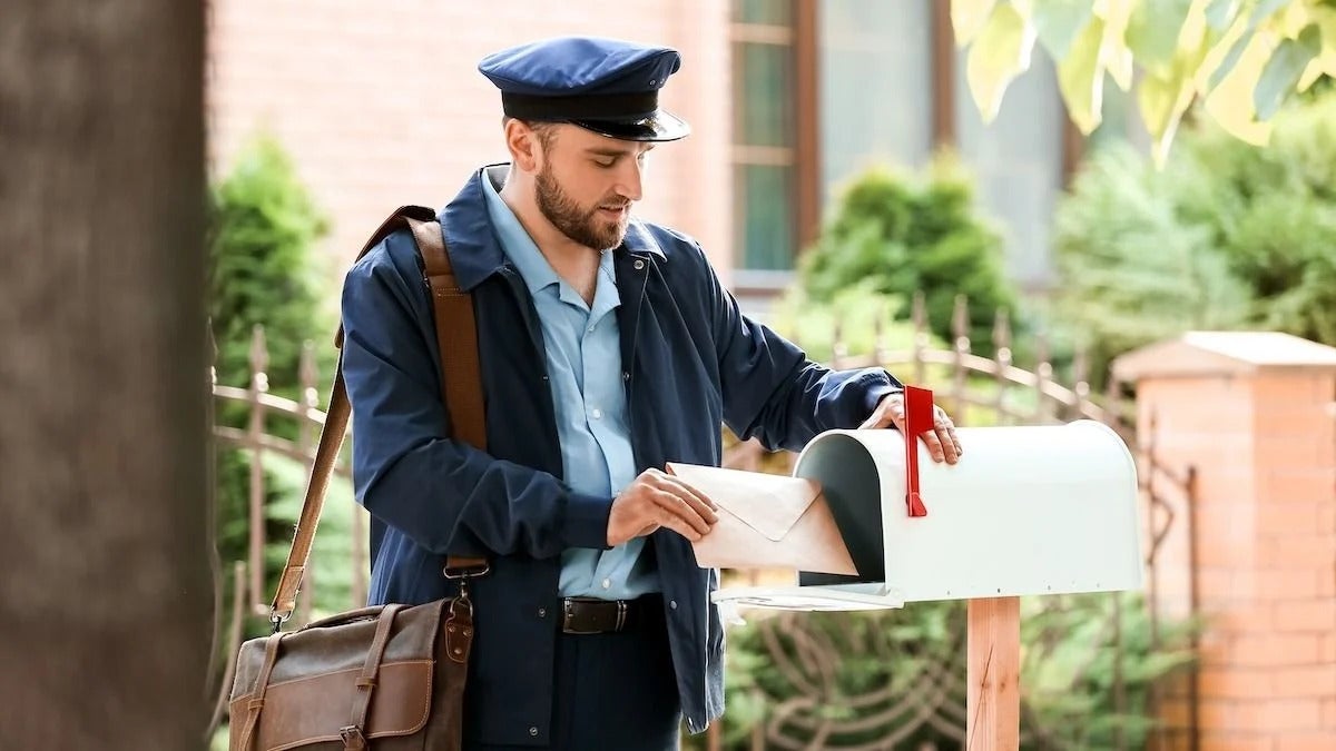 Picture of a mailman putting an envelope into a mailbox