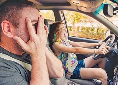 young teen driving car with father in the pasenger seat covering his eyes in fear